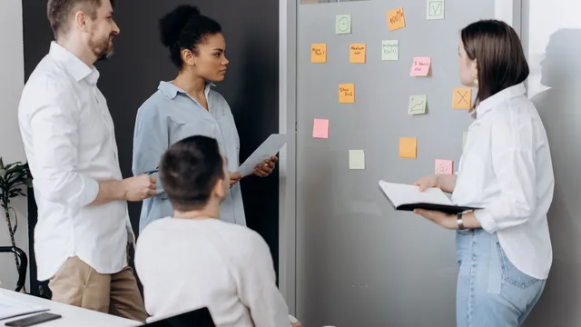 Team sammelt im Besprechungsraum Ideen auf Haftnotizen an einer Glaswand