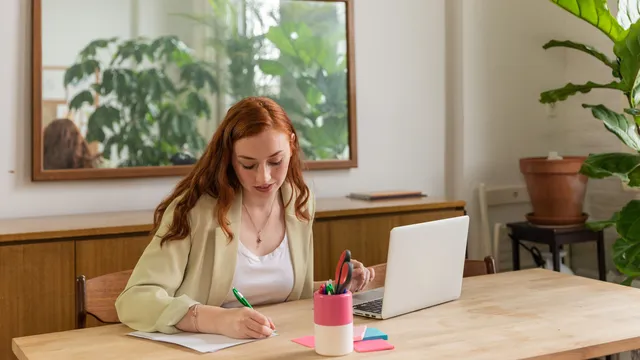 Mitarbeiterin arbeitet am Schreibtisch mit Laptop und Notizblock
