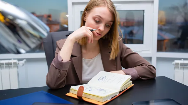 Eine Frau sitzt nachdenklich am Schreibtisch, vor ihr ein aufgeschlagenes Notizbuch.