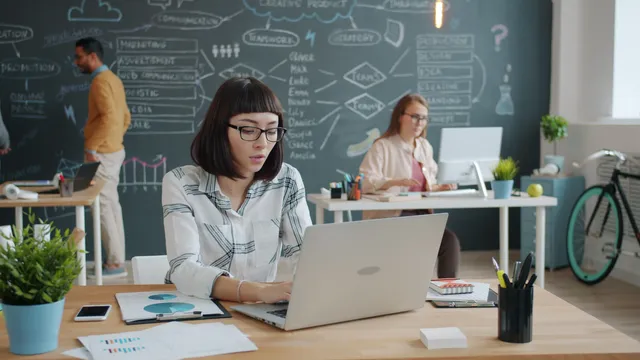 Helles Büro, eine Frau arbeitet am Laptop, im Hintergrund eine Tafel mit Skizzen
