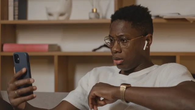 Ein Mann mit Brille sitzt auf dem Sofa und schaut skeptisch auf das Video in seinem Smartphone