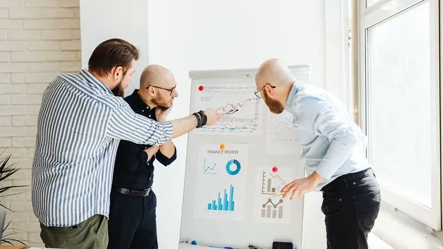 Drei Kollegen besprechen in einem hellen Büro Diagramme auf einem Flipchart
